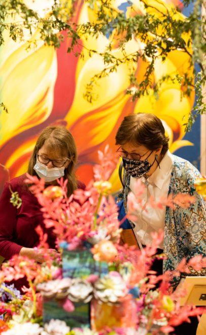 Two women looking at bright colored floral arrangments.