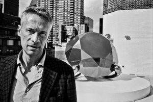 Black and white photo of a white male in front of a statue on a rooftop.