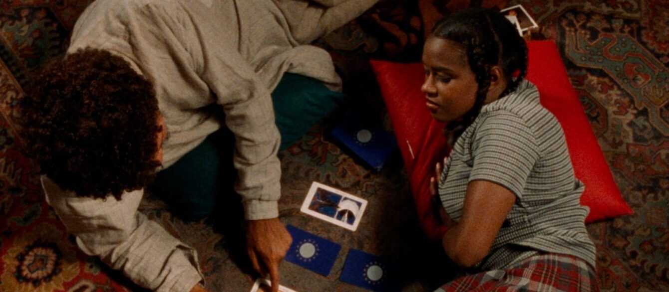 A film still from Drylongso with a young man and a young woman looking at Tarot cards.