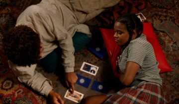 A film still from Drylongso with a young man and a young woman looking at Tarot cards.