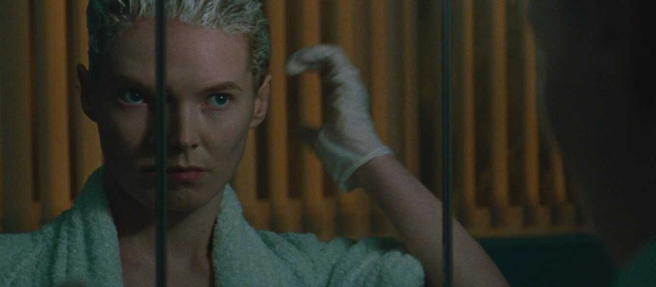 A film still from Blue Jean featuring Rosy McEwen looking in a mirror as she dyes her hair blond.