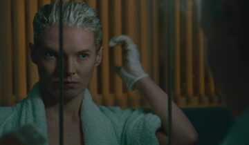 A film still from Blue Jean featuring Rosy McEwen looking in a mirror as she dyes her hair blond.