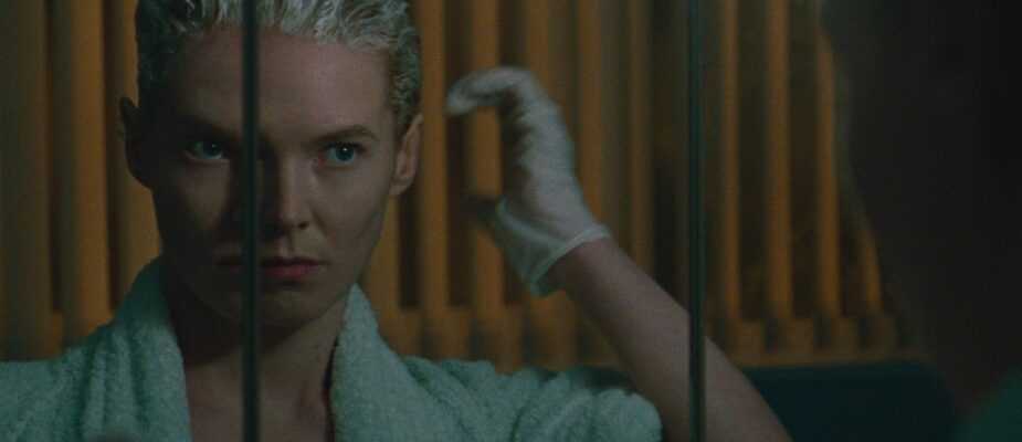 A film still from Blue Jean featuring Rosy McEwen looking in a mirror as she dyes her hair blond.
