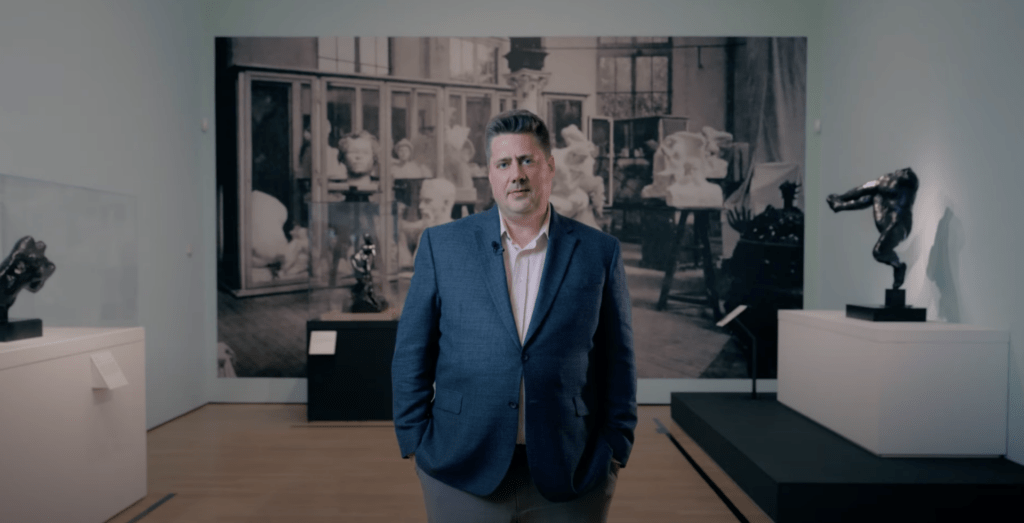 President and CEO Michael J. Anderson standing in an art gallery with Auguste Rodin pieces in the background.