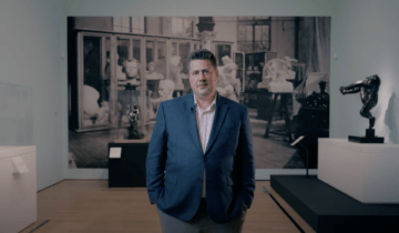 President and CEO Michael J. Anderson standing in an art gallery with Auguste Rodin pieces in the background.