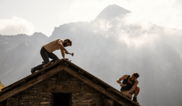 The Eight Mountains Film Still A man hammers a nail into the roof of a house in front of a misty mountain. Courtesy of Sideshow and Janus Films