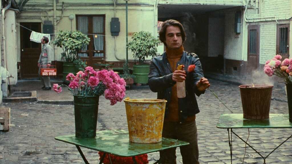 A film still from Bed and Board with Antoine Doinel spraying a flower with water.