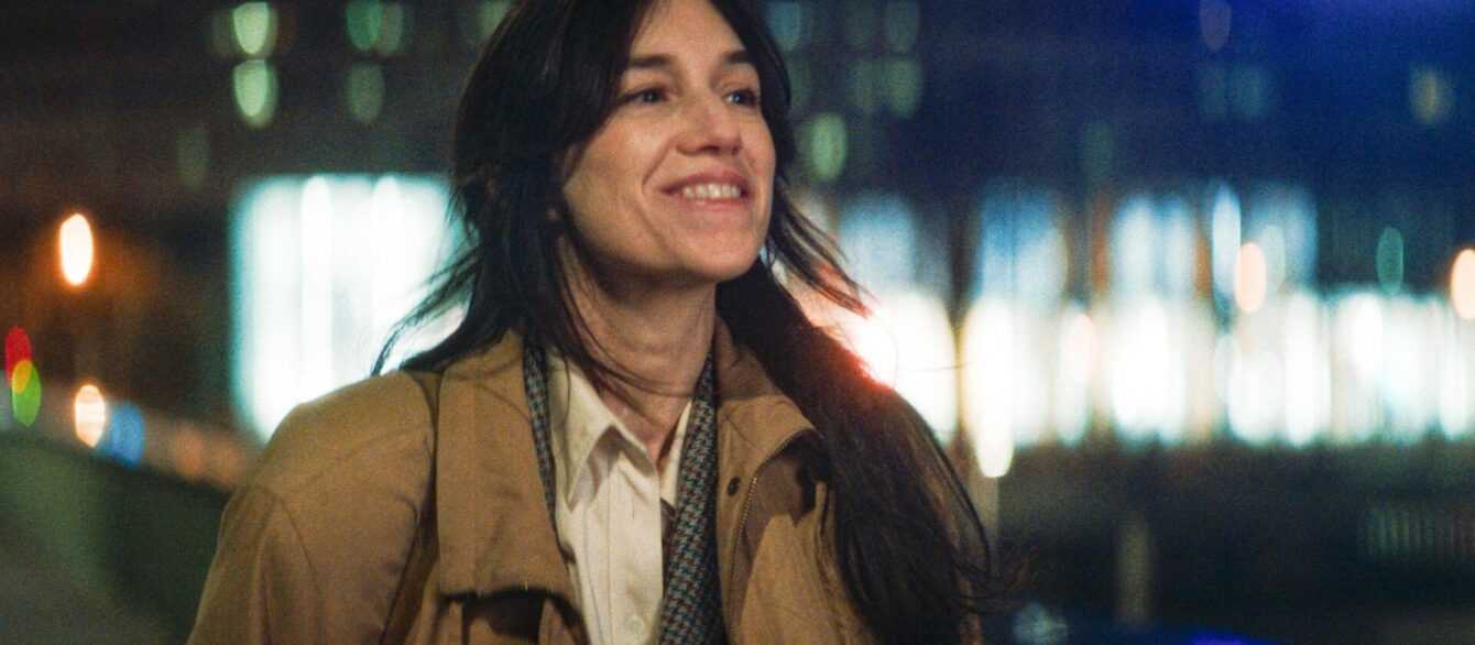 A film still Passengers of the Night with Charlotte Gainsbourg walking and smiling against a nighttime cityscape.