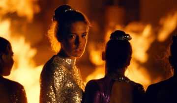 A film still from the The Five Devils of Adèle Exarchopoulos in a gymnastics uniform with flames behind her.