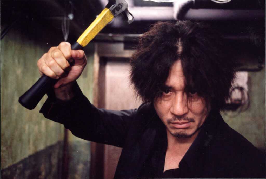 A film still from Oldboy with a man brandishing a hammer.