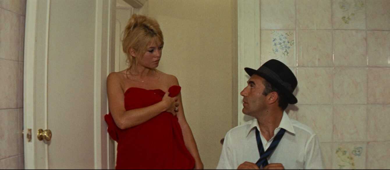 A Film Still from Contempt with a man in a black hat looking up at a blond woman wrapped in a red towel.