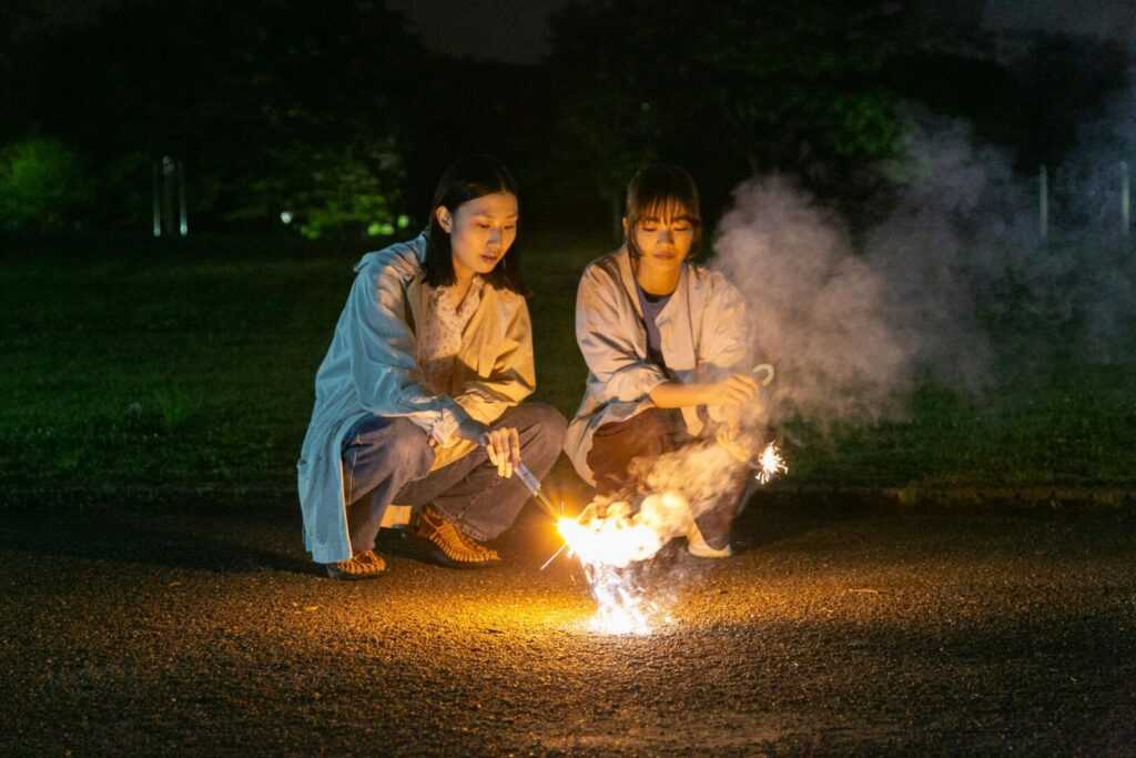 A film still from Remembering Every Night with two young women holding sparklers.