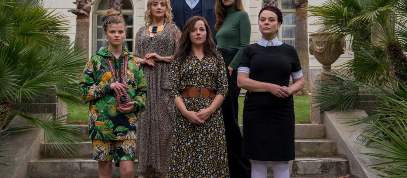 Film still from the Origin of Evil with a group of people standing on the steps of a large house