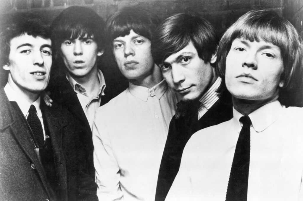 A black and white publicity photograph of the Rolling Stones with Brian Jones at the right edge of the frame.