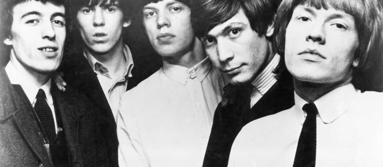 A black and white publicity photograph of the Rolling Stones with Brian Jones at the right edge of the frame.
