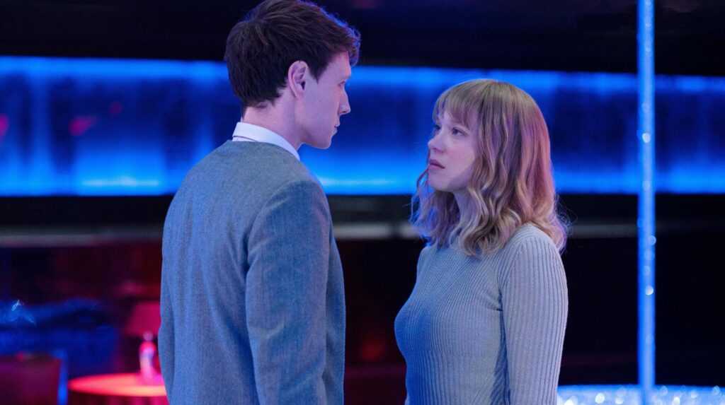 THE BEAST Photo1 © Carole Bethuel. A man (George MacKay) and woman (Léa Seydoux) stand close together in the middle of a nightclub, staring at each other.
