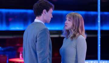 THE BEAST Photo1 © Carole Bethuel. A man (George MacKay) and woman (Léa Seydoux) stand close together in the middle of a nightclub, staring at each other.