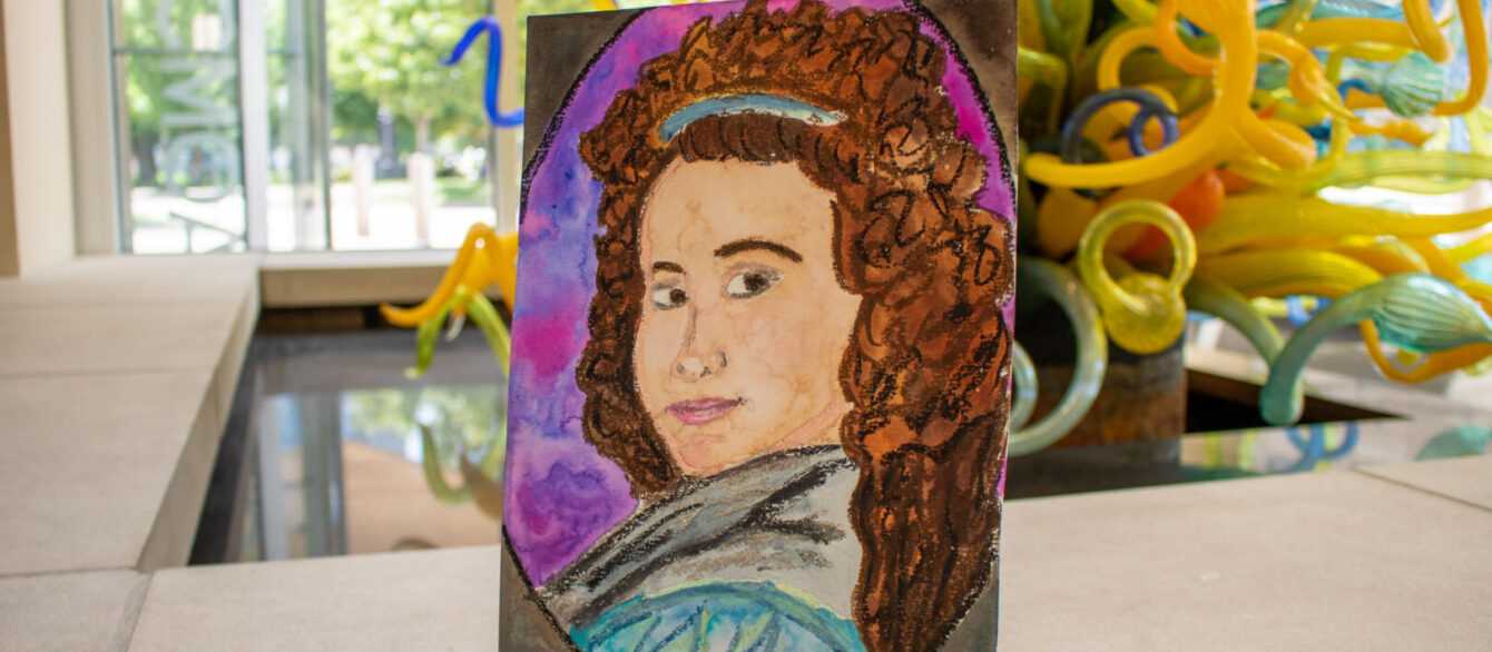 A painted portrait displayed on a small easel sits inside the museum with colorful glass artwork visible in the background.