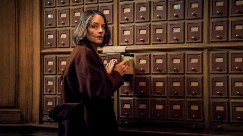 A woman stands in front of a wall of library card catalog drawers while opening a drawer in a scene from A Private Life.