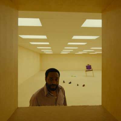 A man stands in a brightly lit, nearly empty room in a still image from the film Backrooms.