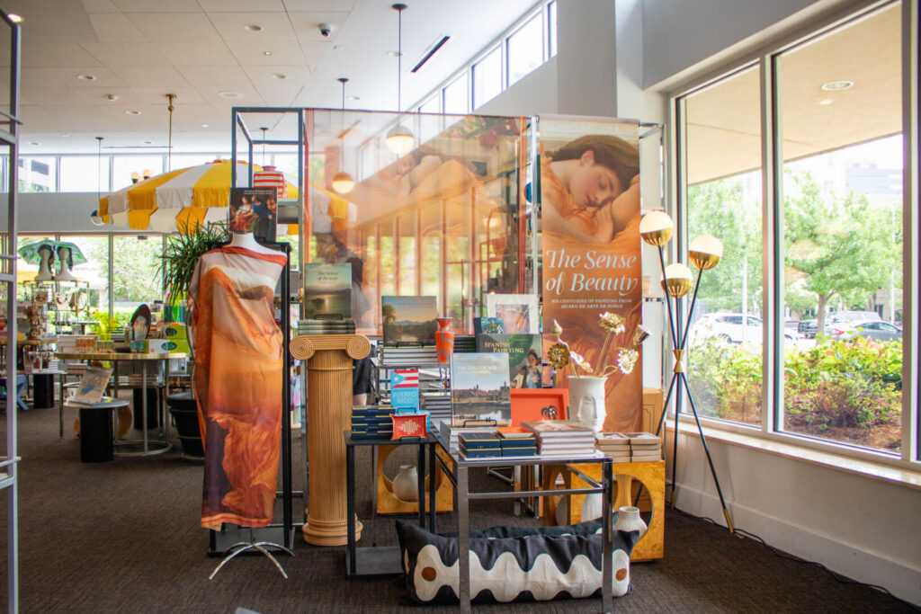 Museum store display featuring The Sense of Beauty merchandise, books, textiles, and decorative displays near large windows.