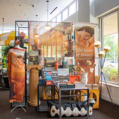 Museum store display featuring The Sense of Beauty merchandise, books, textiles, and decorative displays near large windows.
