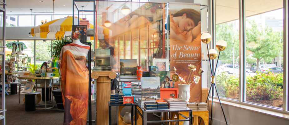 Museum store display featuring The Sense of Beauty merchandise, books, textiles, and decorative displays near large windows.